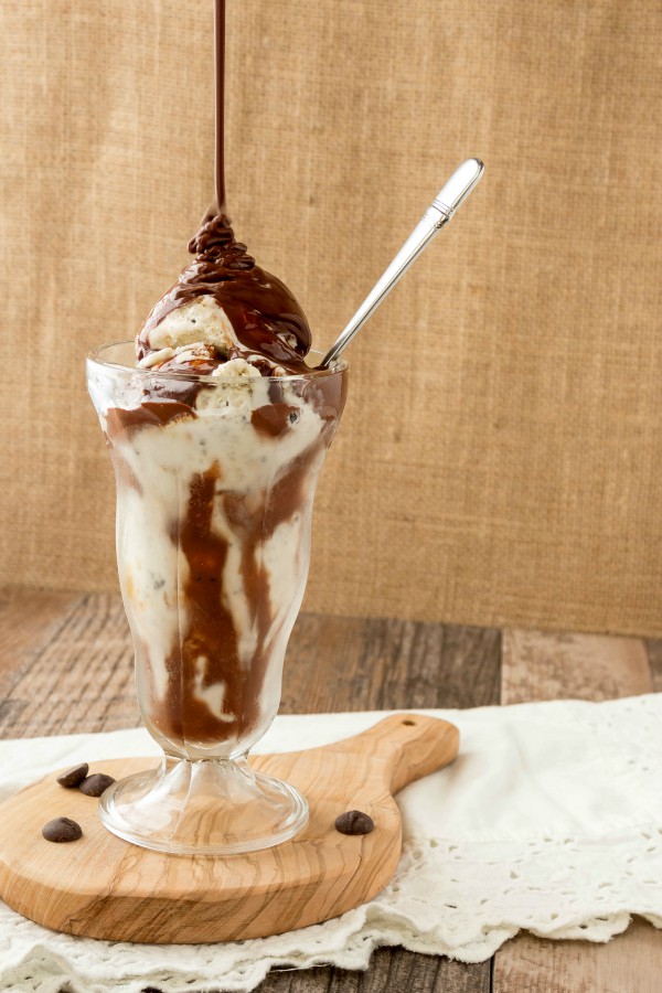 hot chocolate sauce pouring over a sundae glass of ice cream