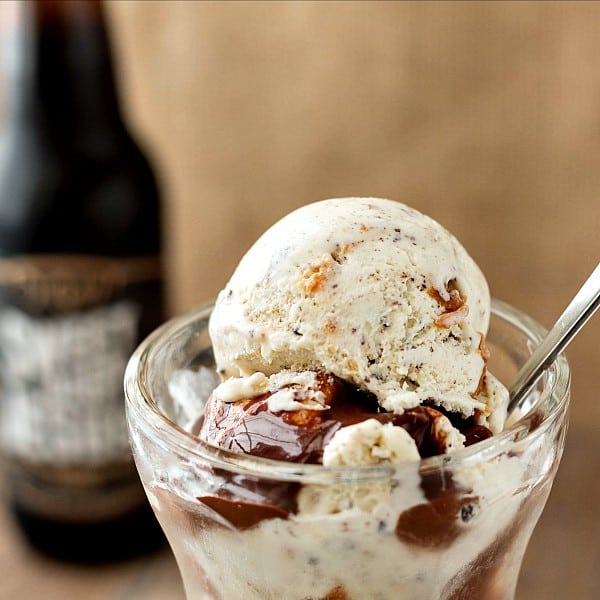A close up of scoops of ice cream with chocolate peanut butter sauce poured over and an out of focus beer bottle in the background.