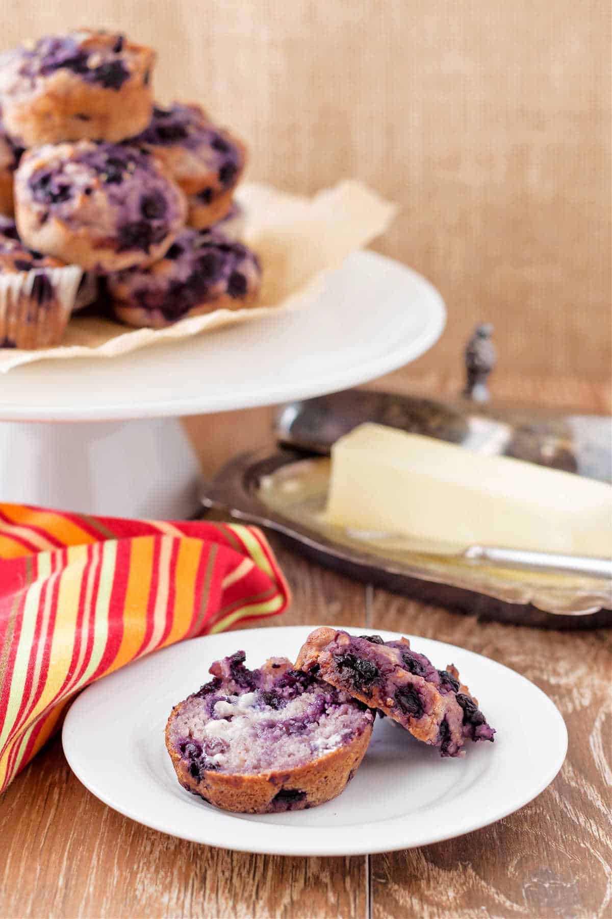 A dairy free blueberry muffin split in half next to a dish of butter. 