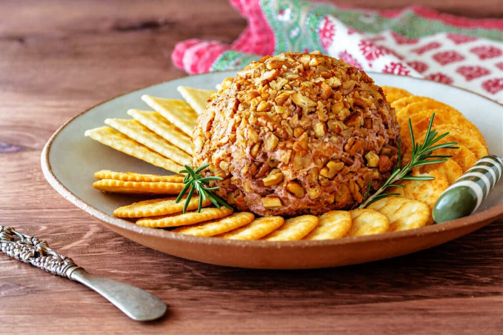 A pecan-crusted cheeseball on aplate with crackers.