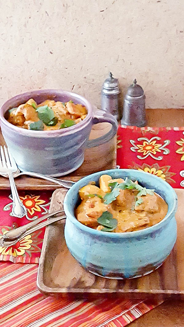 A bowl Tikka masala with homemade paneer in a pottery bowl on a wooden plate. 