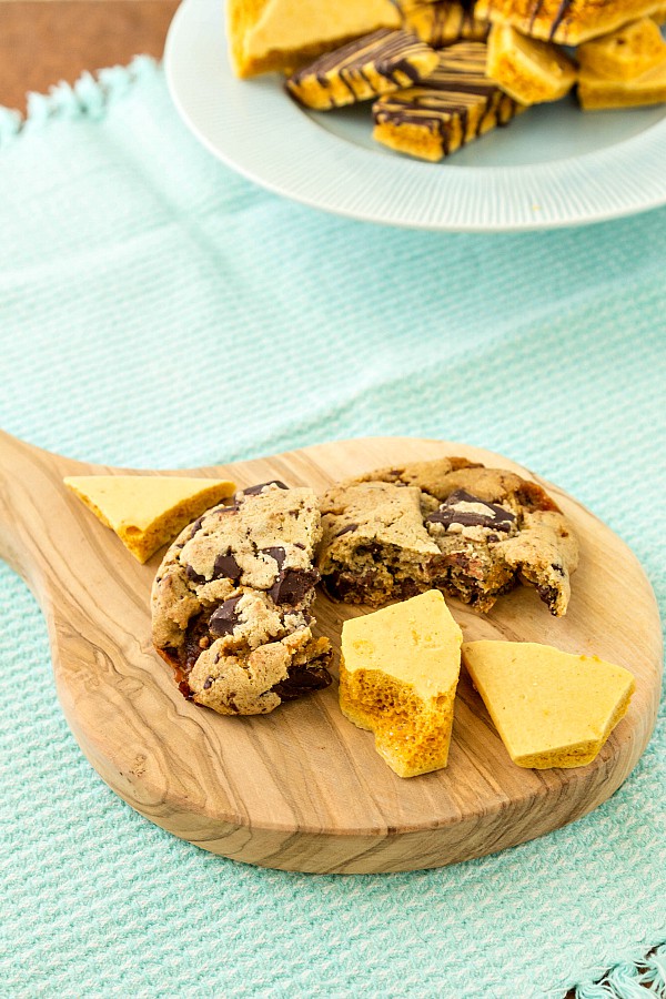 Wooden cutting board with bourbon honeycomb candy and Bourbon Honeycomb Chocolate Chunk Cookies.