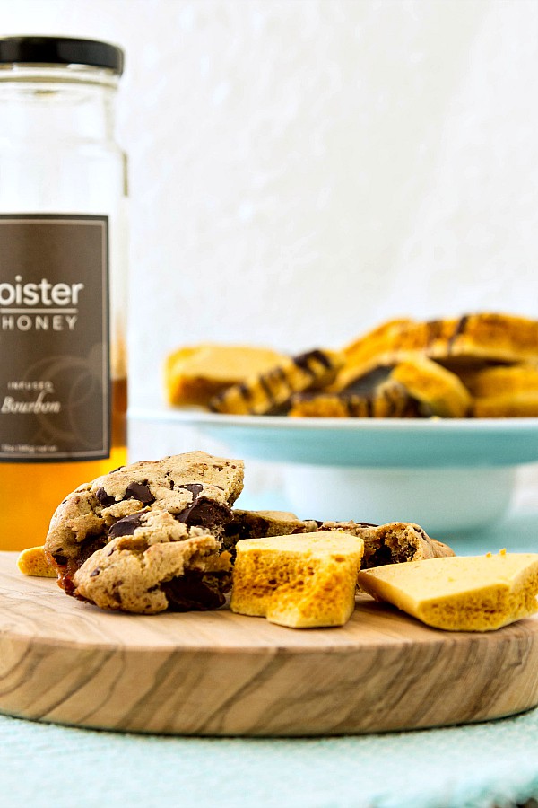 Cookies and honeycomb candy on a wooden board with a jar of bourbon-infused honey and more honeycomb candy in the background.