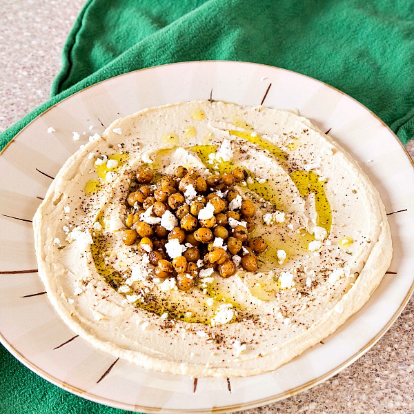 A plate spread with hummus and topped with roasted chickpeas, olive oil. feta and za'atar.