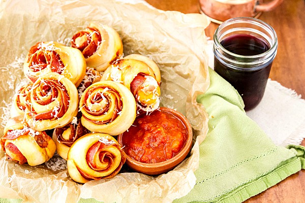 A basket of spicy pinwheel appetizers with marinara for dipping.