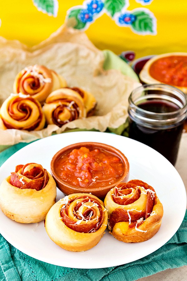 Pizza pinwheels on a plate with marinara for dipping.