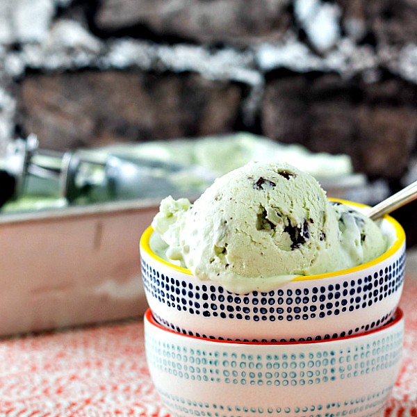 A dish of mint chip ice cream in front of a metal container of ice cream.