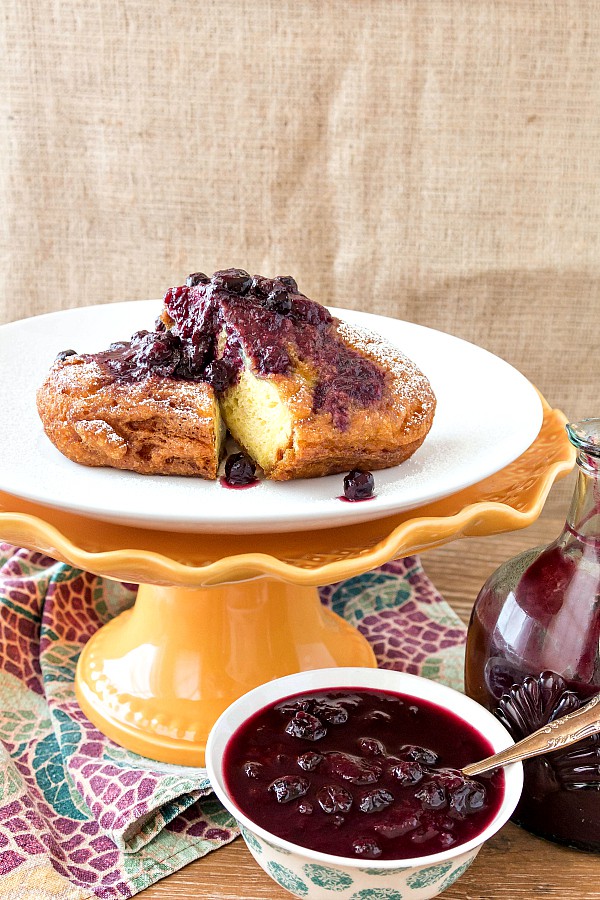 Deep fried french toast with peach blueberry sauce served on a footed cake stand.