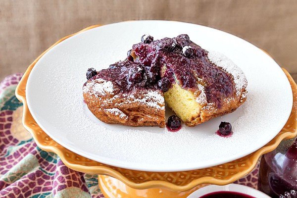 Sliced french toast with whole blueberry and peach sauce and some powdered sugar on top, One slice is missing.