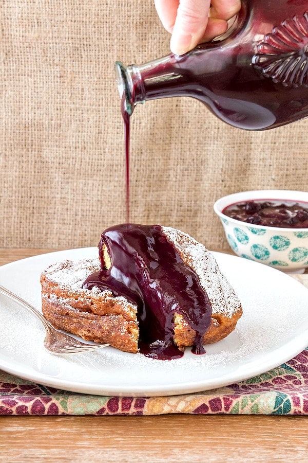 Pour shot of blueberry peach sauce pouring over sliced deep fried french toast.