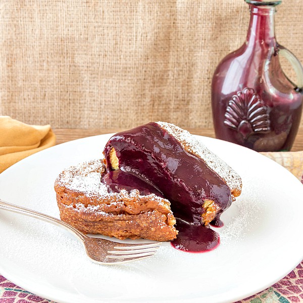 A thick slice of french toast with pureed berry sauce on a white plate and a sprinkle of powdered sugar.