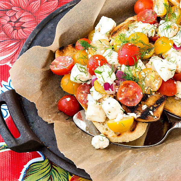 A cast iron pan with a layers of parchment paper and Dill Caprese Bruschetta on top.