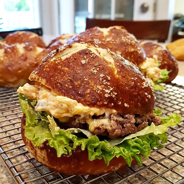 "A close up of a burger served on a pretzel bun. The coarse salt is clear on the brown top of bun.