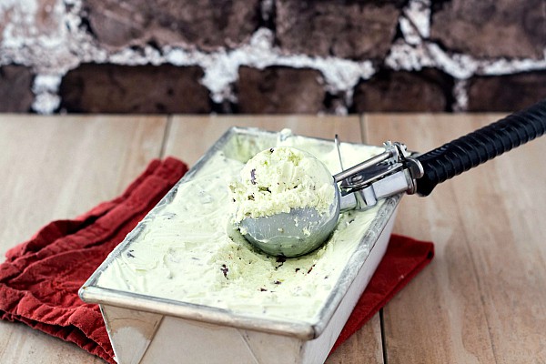 Metal rectangular container of pale green mint chip ice cream with a scoop in the container.