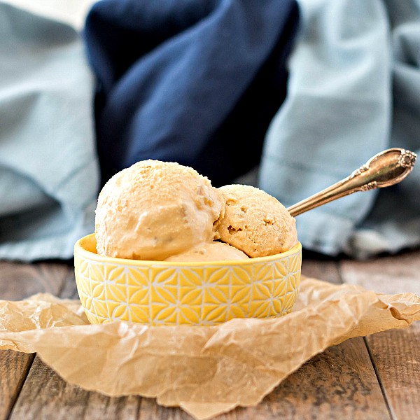 A yellow bowl of Smoked Caramel Pineapple Ice Cream with a silver spoon, sitting on a wooden table.
