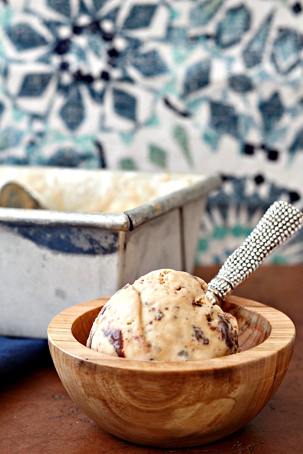 A wooden bowl of Salted Caramel Turtle Fudge Swirl Ice Cream with a metal spoon.