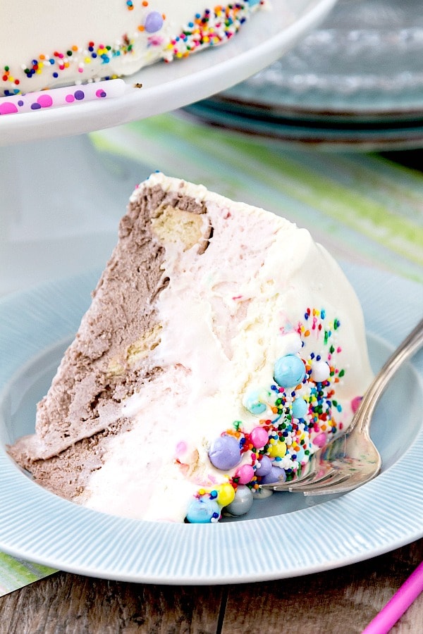 A slice of Neapolitan ice cream cake decorated with sprinkles and pearls on a blue plate.