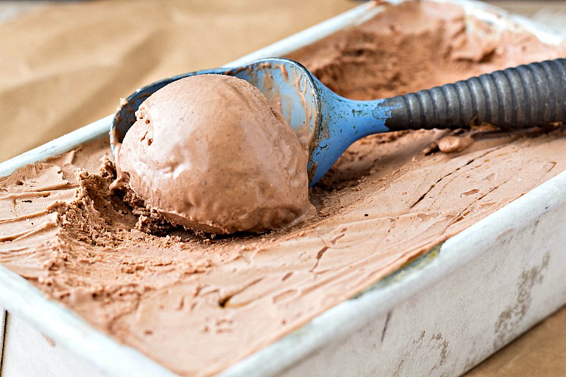 A metal container of chocolate ice cream with an ice cream scoop in it.