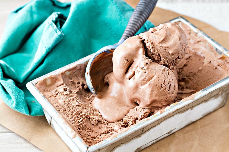 A container of chocolate ice cream with a couple of partially melted scoops in it.
