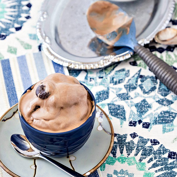 A bowl and spoon of Junior Mint Chocolate Ice Cream on a blue, white and green table cloth. 