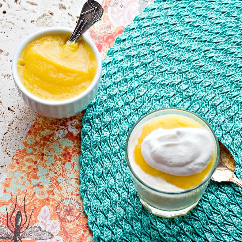 One serving of  mango pineapple fool  next to a bowl of pineapple mango puree on a turquoise placemat.