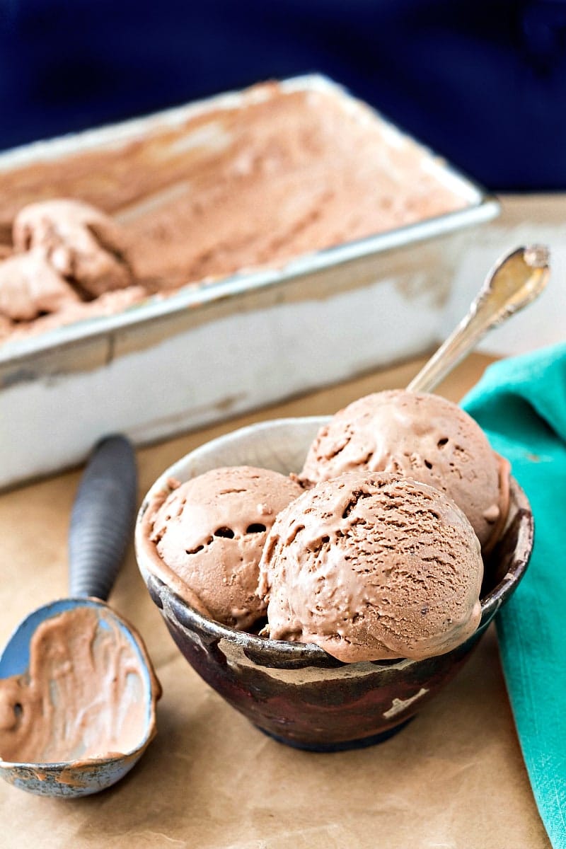 A bowl of chocolate caramel ice cream with a spoon in it and the container of ice cream in the background.