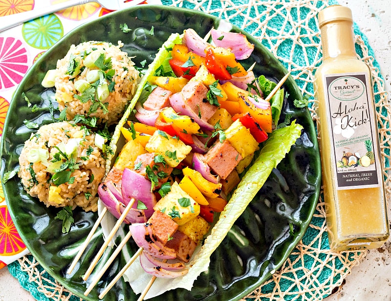 A plate of Hawaiian Pineapple Ham Skewers with Sweet and Hot Pineapple Rice next to a bottle of Tracy's Gourmet Aloha Kick Dressing.