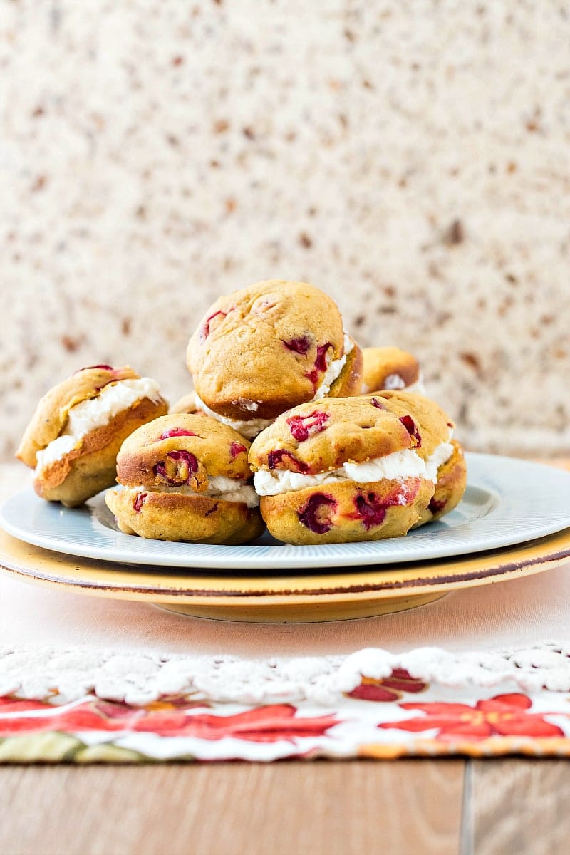 A pile of pumpkin whoopie pies with cranberries on a white plate.