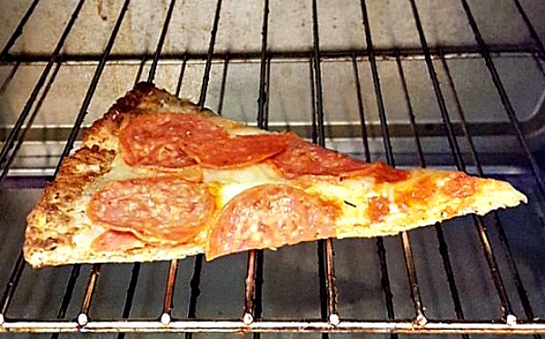 A piece of cauliflower pizza crust pizza heating up on a rack in the oven.