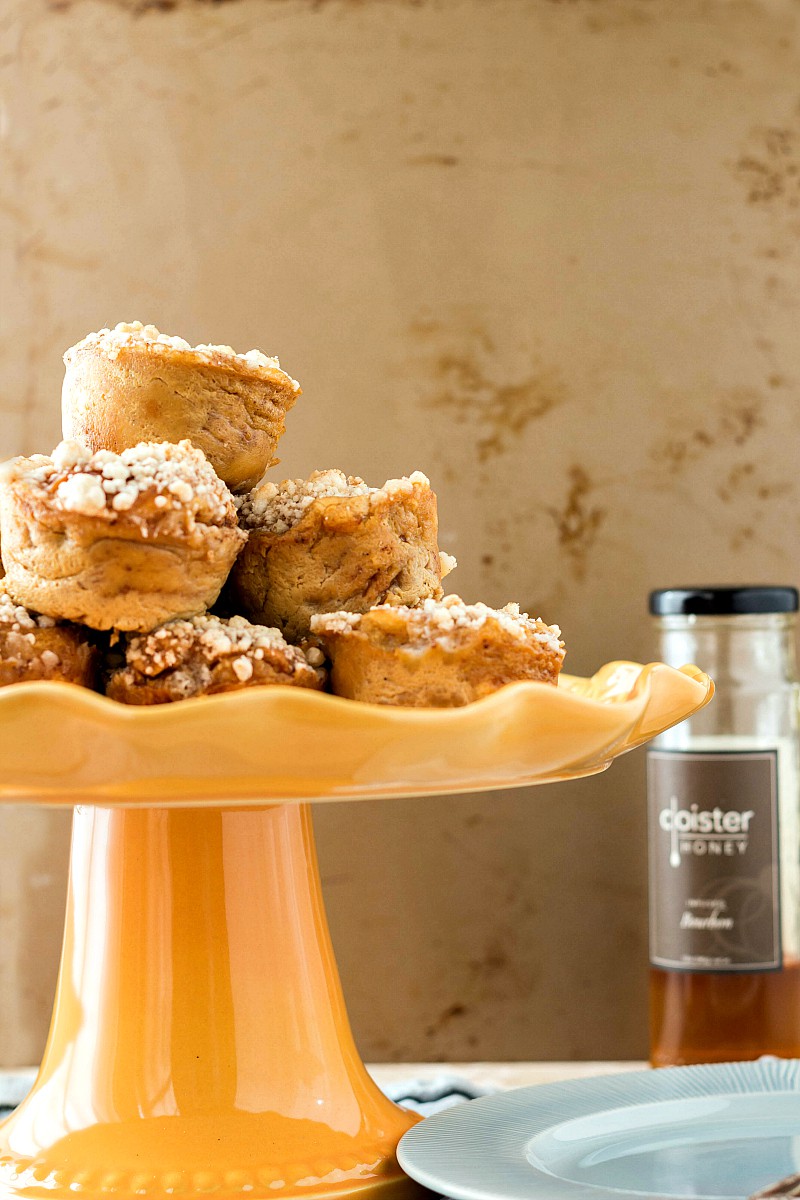  Hawaiian Roll French Toast Muffins stacked on a yellow footed cake stand near a jar of honey.