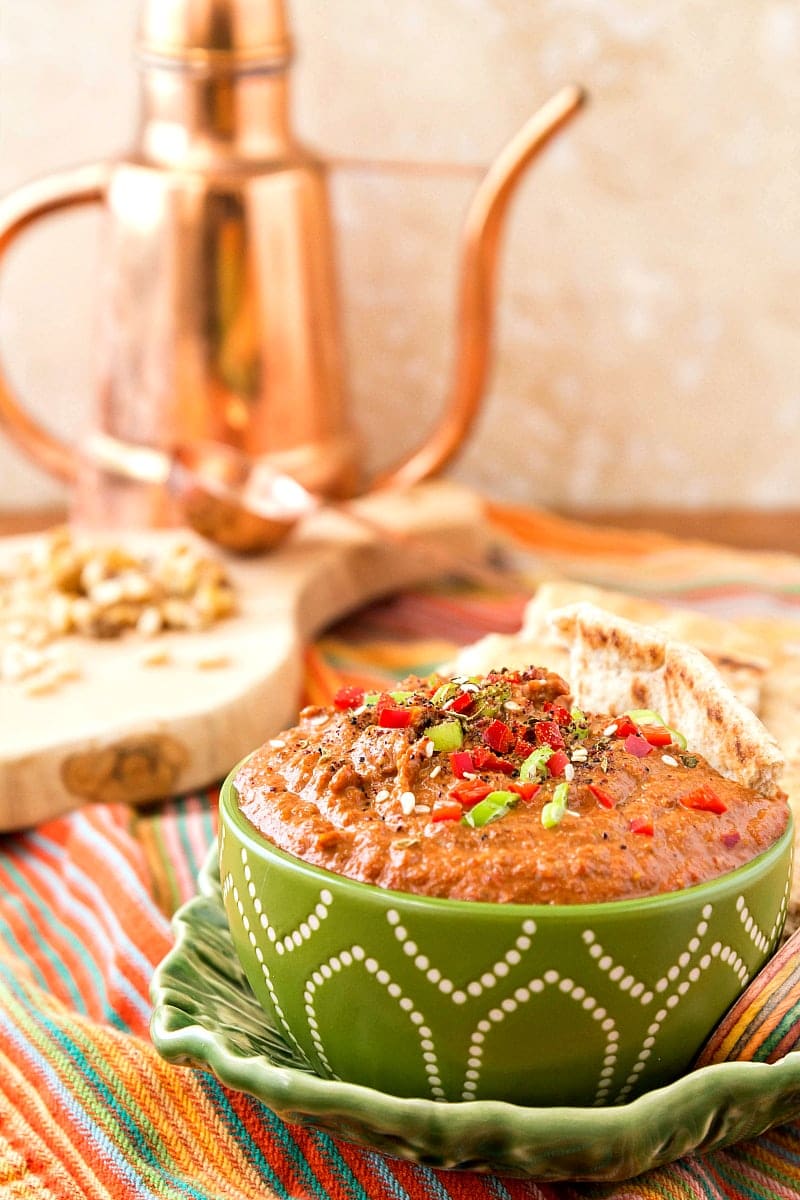 A bowl of middle eastern walnut dip garnished with green onion and peppers with pita.