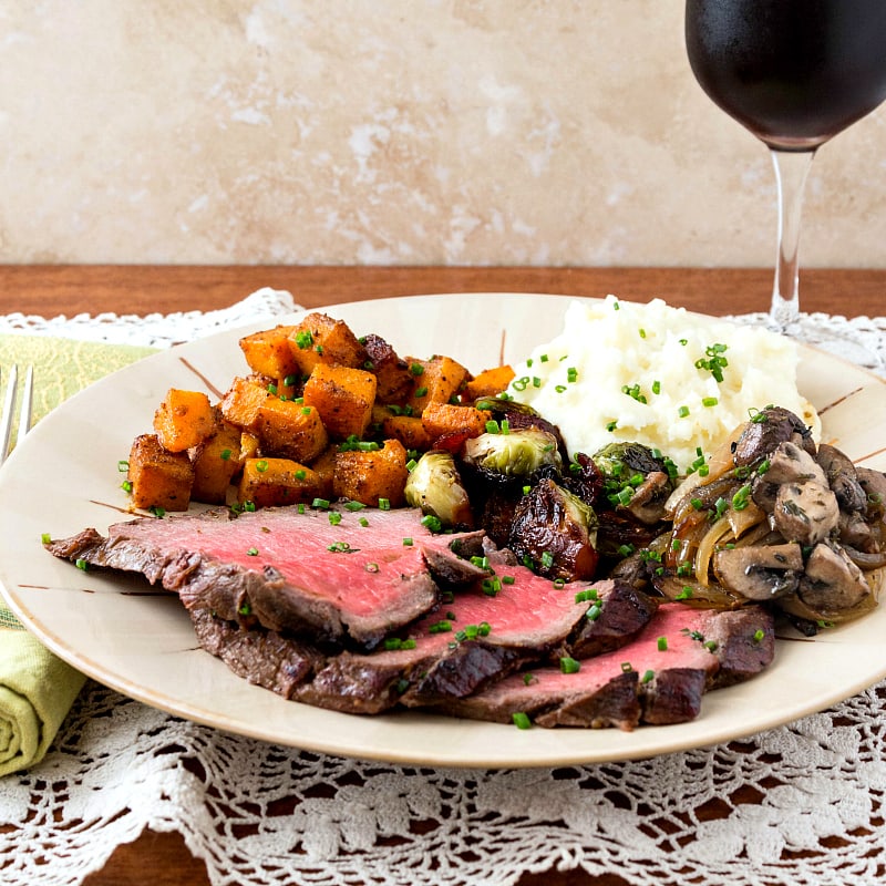 Meal with rare london broil on plate and a glass of red wine.
