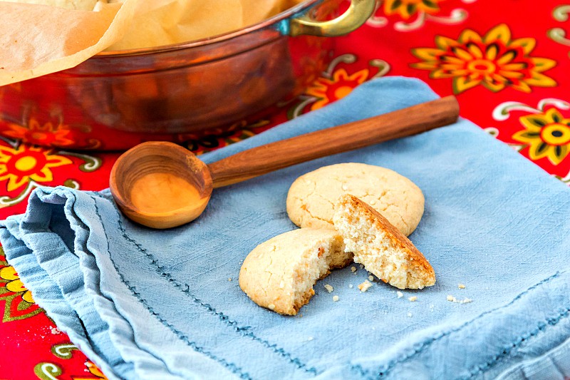 A broken ghoriba bahla cookie on a blue napkin with a wooden spoon.