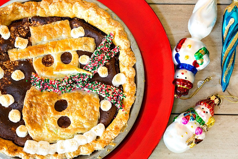 A Mexican hot chocolate pie with snowman crust applique and snowman ornaments alongside.