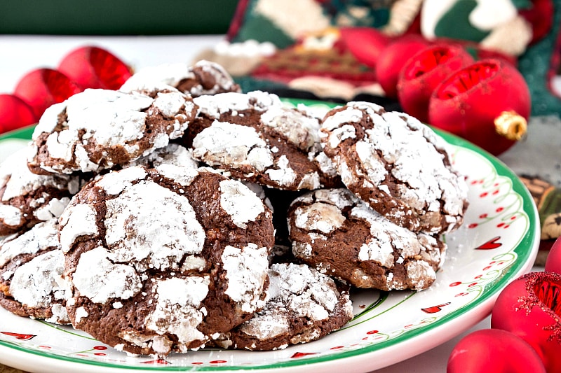 A  pile of gluten-free Christmas cookies on a plate, surrounded by red Christmas ornaments.