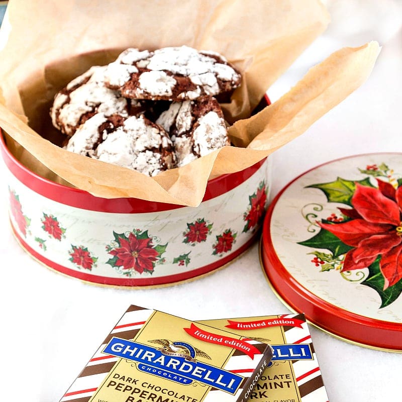A holiday tin, decorated with poinsettias  of gluten free chocolate cookies with 2 bars of peppermint bark.