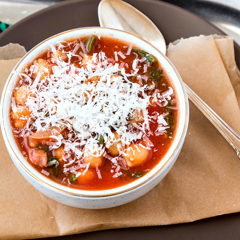 A white bowl of easy Italian sausage soup with shaved Parmesan on top.