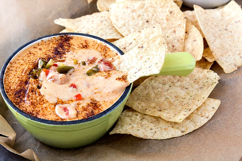 A small green cast iron pan with homemade nacho cheese in it and chips on the side.