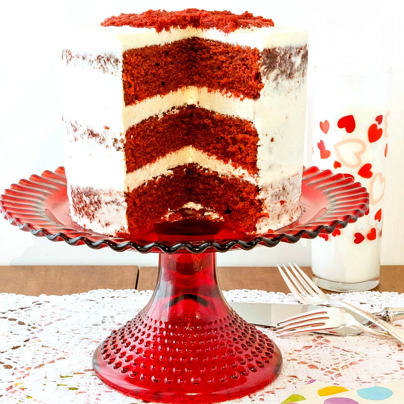 A three layer traditional red velvet cake with ermine frosting. One slice has been removed showing red interior.