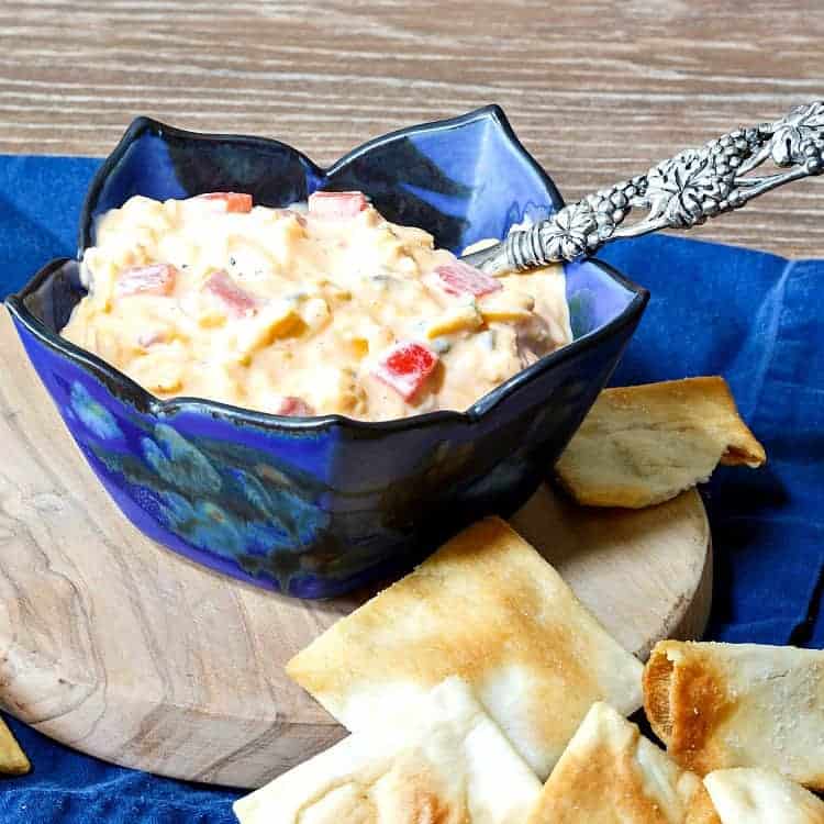 Close up of a blue bowl of spicy smoked pimento cheese spread with a metal spoon ready for serving.