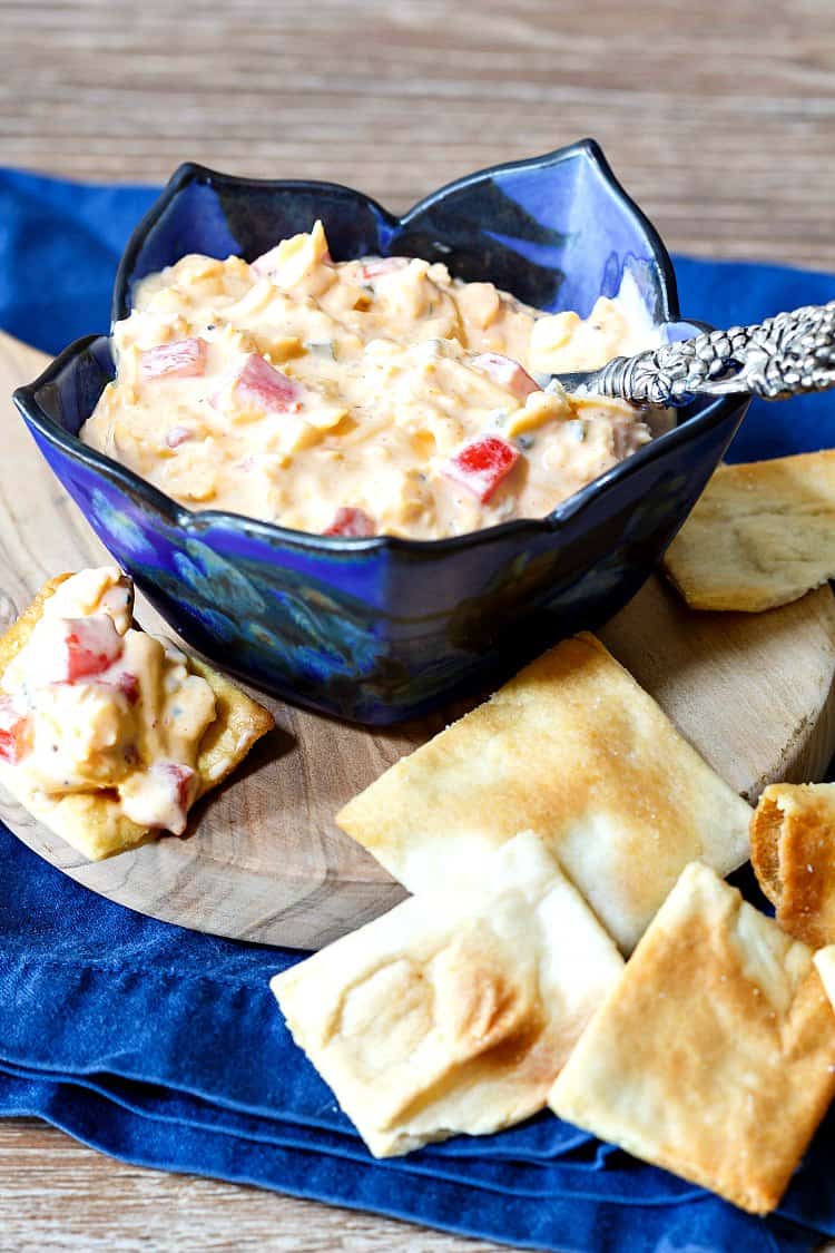 Spicy smoked pimento cheese spread in a blue bowl with rectangular pita crackers.