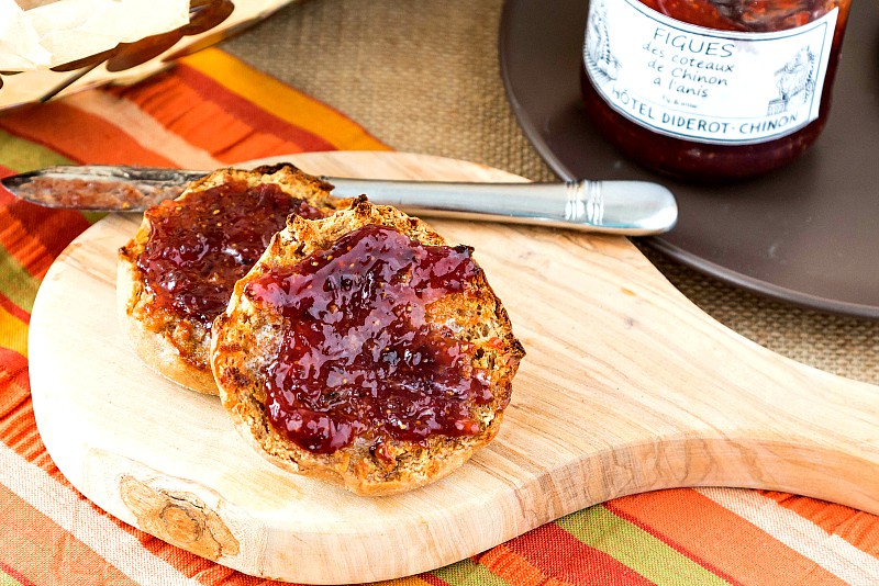 A split, toasted sprouted wheat English muffin on a cutting board with jam.