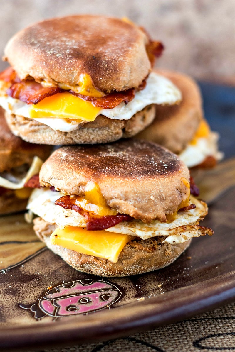 Bacon, egg and cheese sandwiches on sprouted English muffins piled on a platter.