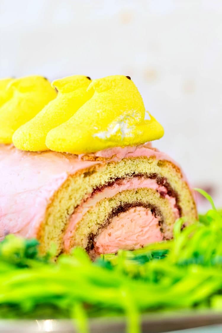 Close up of a jelly roll with pink frosting topped with Yellow Peeps.