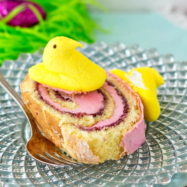 Close up of a slice of pink iced jelly roll on a glass plate topped with a yellow Easter peep.