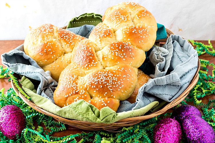 A basket of braided breads for Easter wit green crinkle paper and purple glitter eggs.