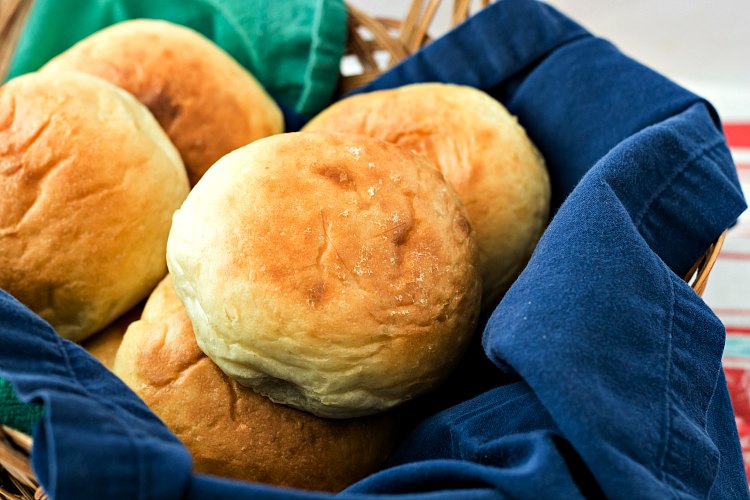 A close up of homemade potato rolls in a basket with dark blue napkin.
