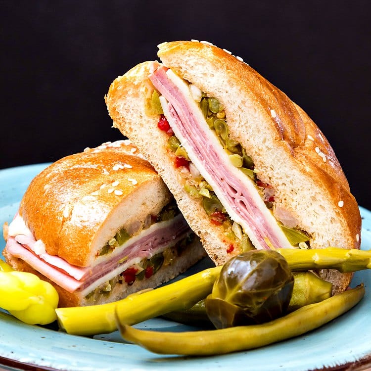 Close up of a NC muffuletta sandwich cut in half served with pickled vegetables.
