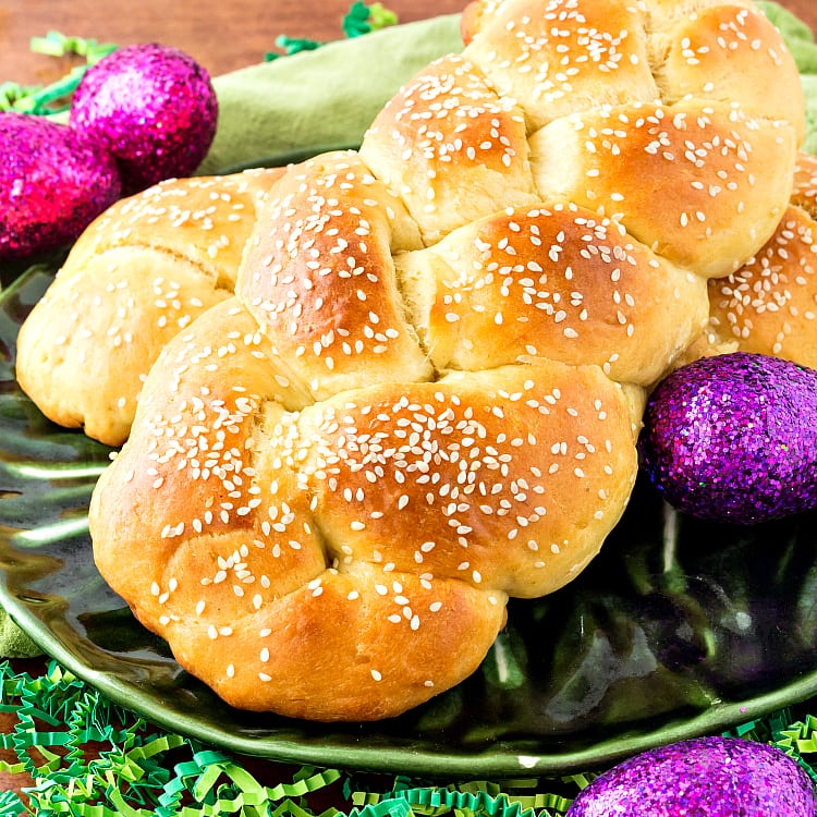 Braided bread topped with sesame seeds on a green plate with purple glitter eggs. 