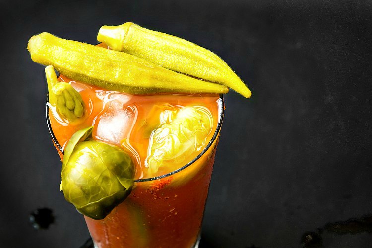 Pickled okra and brussels sprouts garnishing a clear glass full of bloody mary.